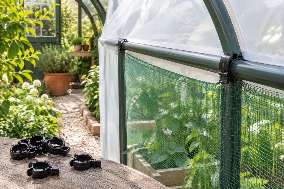 Clips de serrage noirs fixant une toile et un filet sur les tubes d’une serre de jardin.