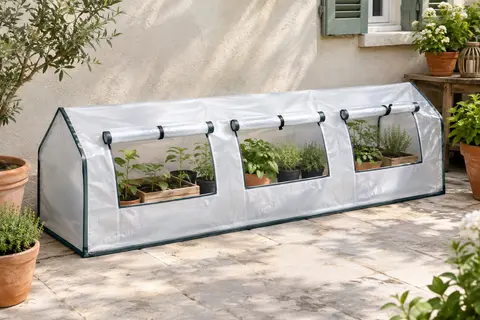 Mini-serre blanche en PE et acier avec trois fenêtres enroulables, installée près d’un mur sur une terrasse