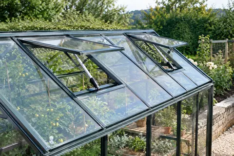 Deux ouvre-fenêtres automatiques en aluminium fixés aux lucarnes d’une serre de jardin vitrée.