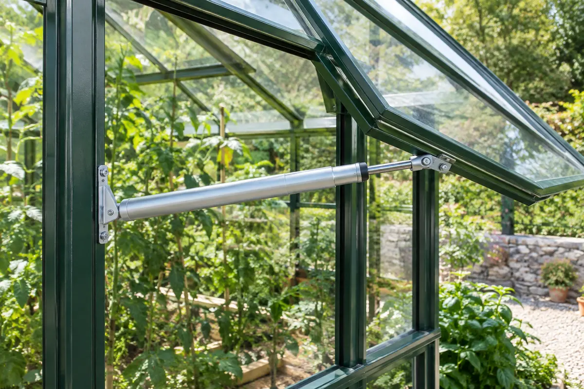 Vérin automatique en acier galvanisé installé sur une fenêtre entrouverte de serre de jardin