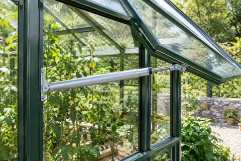 Vérin automatique en acier galvanisé installé sur une fenêtre entrouverte de serre de jardin
